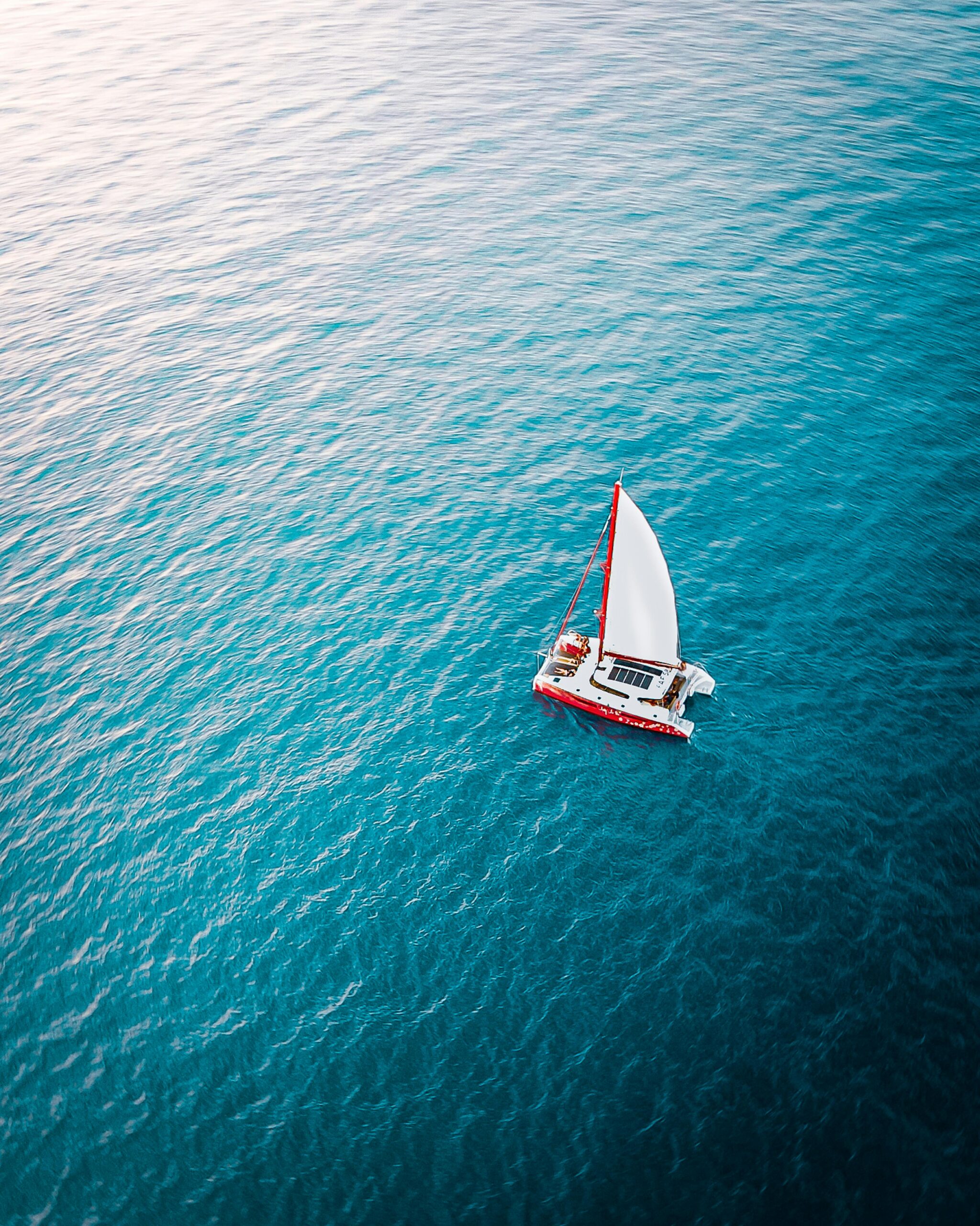 A sailboat sailing across rippling water as seen from above